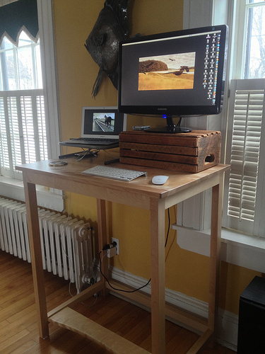 Standing desk with laptop and monitor situated between two windows.